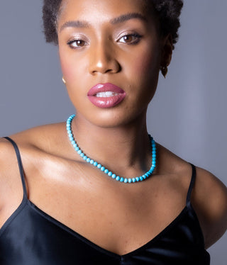 Woman wearing a blue beaded necklace against a gray background