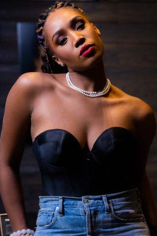 Woman wearing a black strapless top and blue jeans indoors. with pearl necklaces on