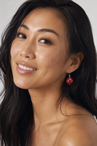 Woman with dark hair and red earrings against a neutral background