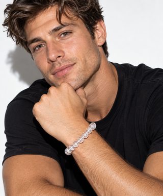A close-up of a man wearing a clear beaded bracelet on his wrist, resting his chin on his hand against a plain white background.