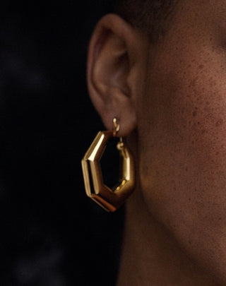 Gold hexagonal earring worn by a person with a dark background