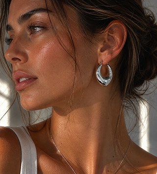 Close-up of a woman wearing silver hoop earrings with a neutral background